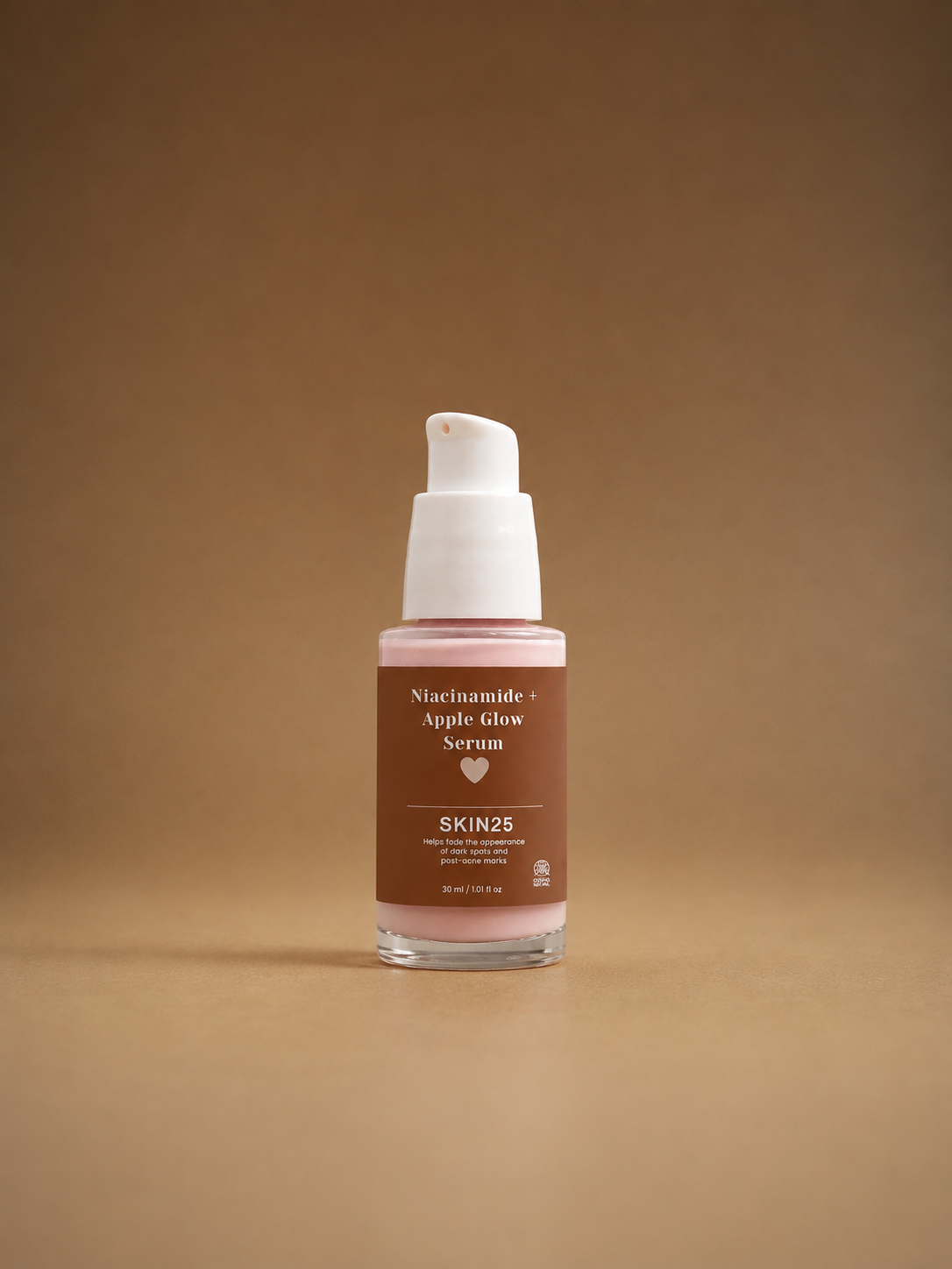A bottle of SKIN25 Niacinamide + Apple Glow Serum with a white pump dispenser and a brown label, set against a solid warm brown background.